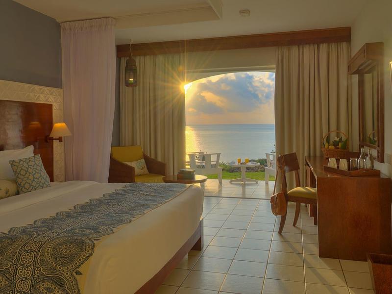 Spacious hotel room with double bed and sea view at sunset.
