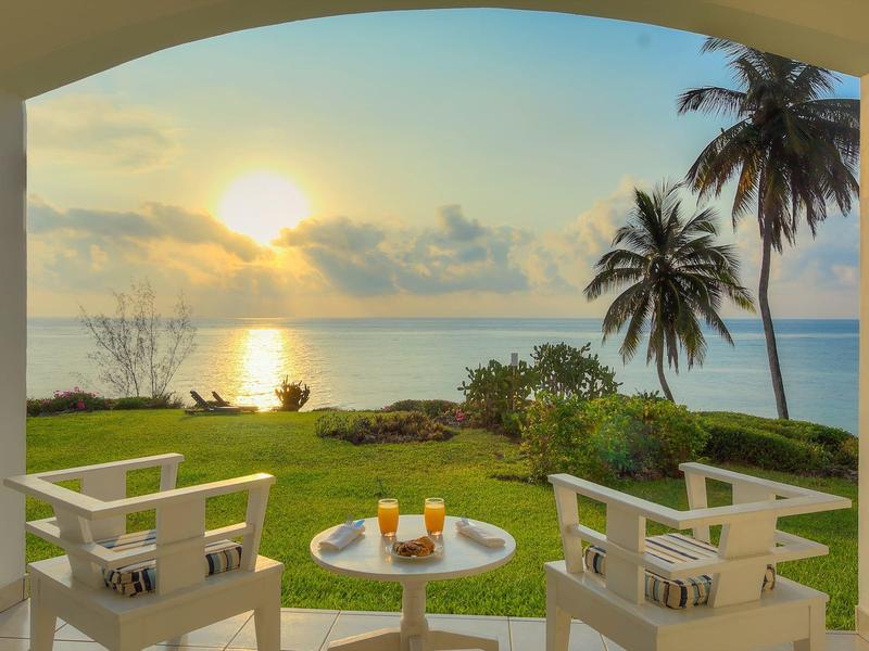 View from a terrace with white chairs and drinks overlooking a sunset over the sea.