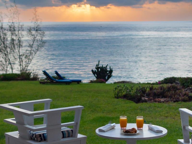 Terrace with white chairs and table, view of sea and sunset under cloudy sky.