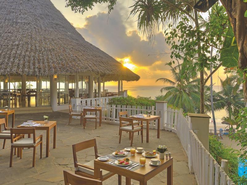 Restaurant terrace with wooden tables and chairs at sunset by the sea.