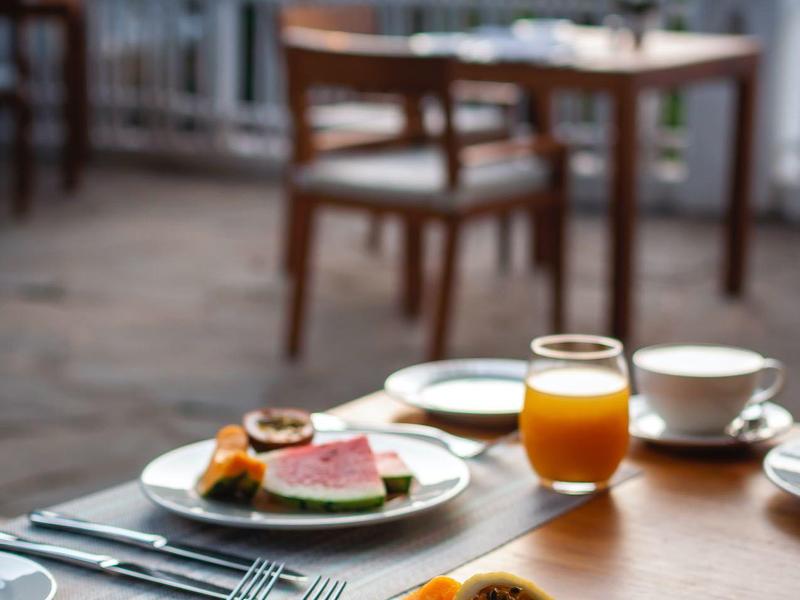 Breakfast table with fresh fruit, juice, and coffee on a terrace with chairs and outdoor view.