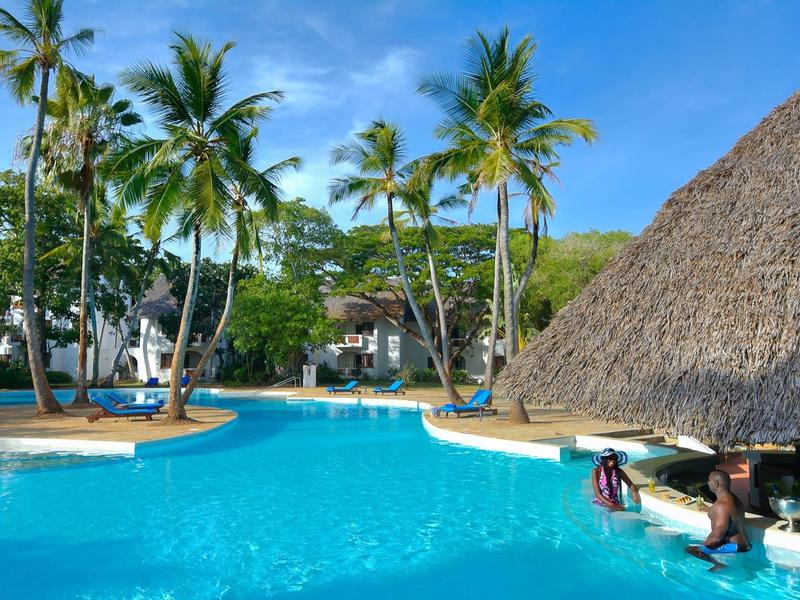 Clear blue pool with palm trees and cozy loungers under a bright blue sky.