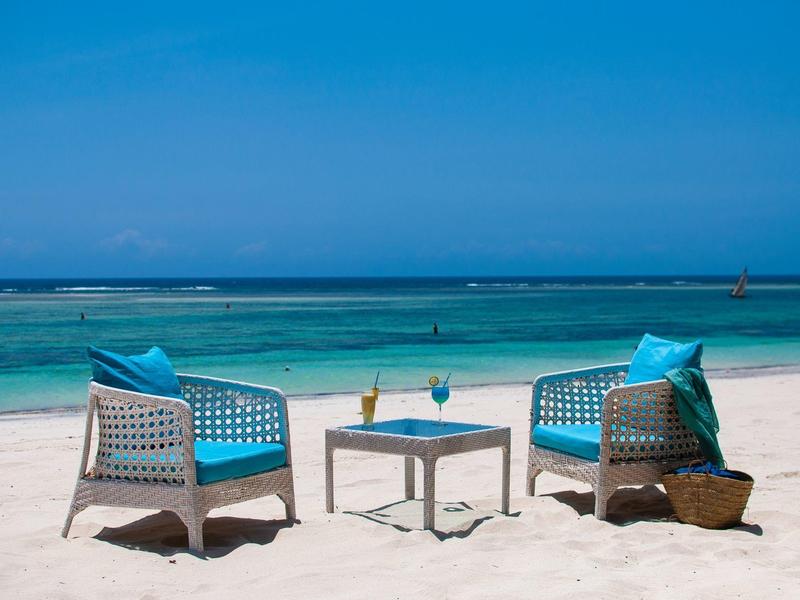 Two blue chairs and a table with drinks on the beach overlooking the sea.