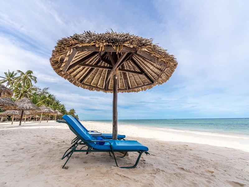 Empty lounge chair under a straw umbrella on a quiet sandy beach overlooking the sea.