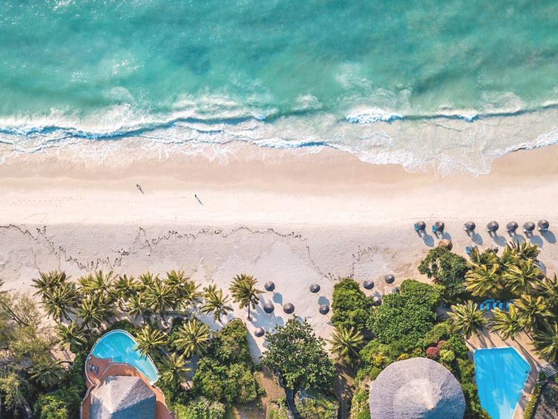 Aerial view of a tropical beach with palm trees, pools, and turquoise water.