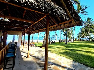 Otwarta chata z dachem ze słomy i krzesłami obok trawiastego terenu blisko plaży.