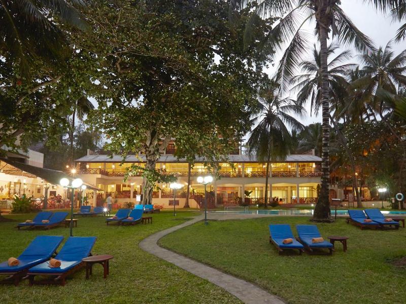 Outdoor view of a hotel with lounge chairs on a lawn and palm trees at dusk.