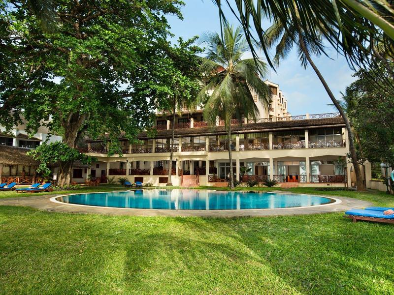 Round pool in a tropical hotel garden with abundant greenery and palm trees.