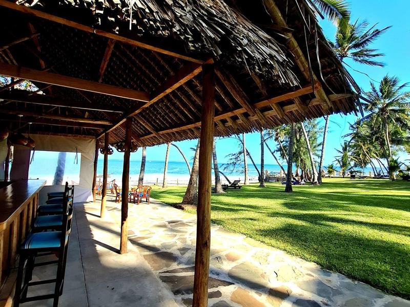 Covered patio with wooden chairs overlooking tropical palm trees and the ocean