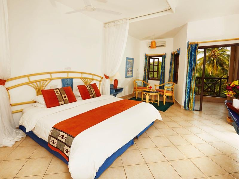 Bright hotel room with large bed, red accents, and access to a terrace.