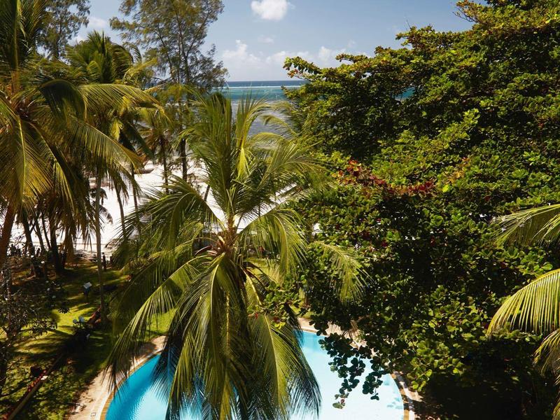 Round-shaped pool surrounded by palm trees and tropical vegetation under a blue sky.