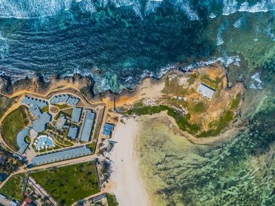 Vue aérienne d'une station avec piscine, plage et falaises boisées au bord de la mer.