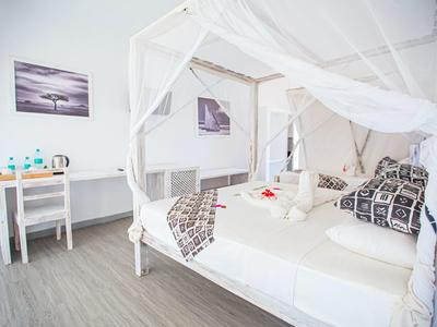 Chambre lumineuse avec lit à baldaquin, décor moderne et table avec bouteilles d'eau.