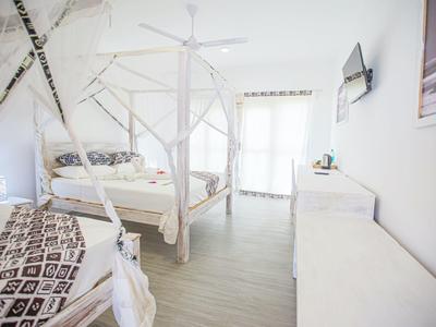 Chambre d'hôtel lumineuse avec plafond incliné, lit à baldaquin et coin salon près de la fenêtre.