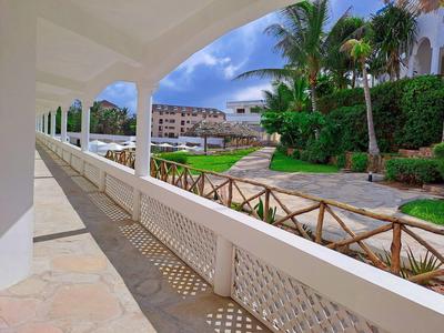 Vue sur la piscine du complexe avec des chaises longues depuis un balcon ombragé avec des colonnes blanches.