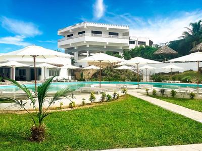 Hôtel moderne avec piscine, parasols et jardin bien entretenu sous un ciel ensoleillé.