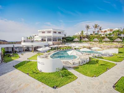 Modernes Hotel mit mehreren Schwimmbädern, Liegestühlen und grünen Rasenflächen unter blauem Himmel.