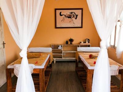 Salle de bien-être accueillante avec deux tables de massage et murs orange chaleureux.