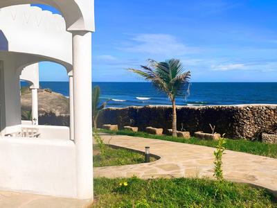 Un bâtiment d'hôtel blanc avec une arche et vue sur la mer et des palmiers sous un ciel bleu.