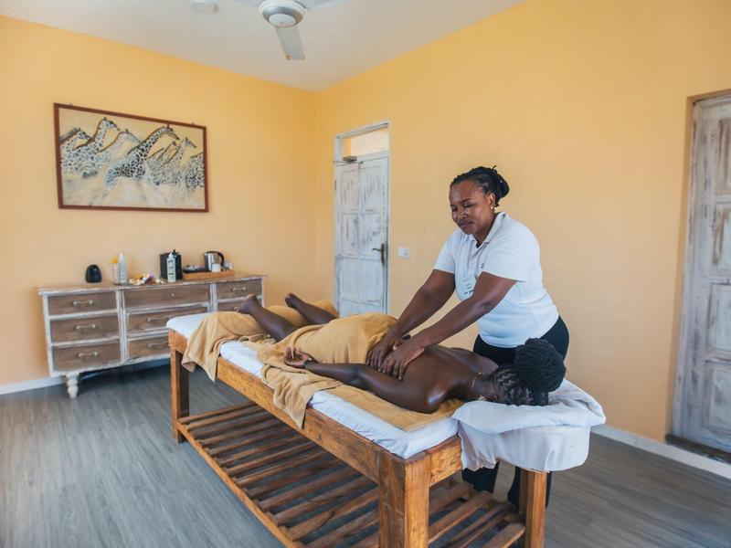 Une femme masse un homme sur une table de massage dans une pièce lumineuse aux murs jaunes.