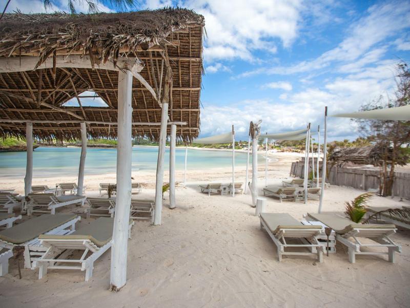 Chaises longues vides sous des toits de paille sur une plage de sable face à la mer.