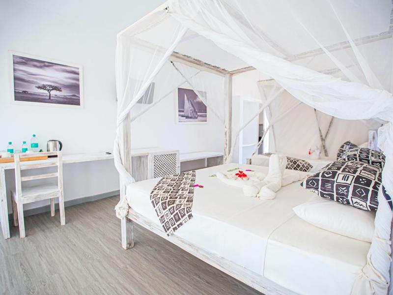 Chambre lumineuse avec lit à baldaquin, décor moderne et table avec bouteilles d'eau.