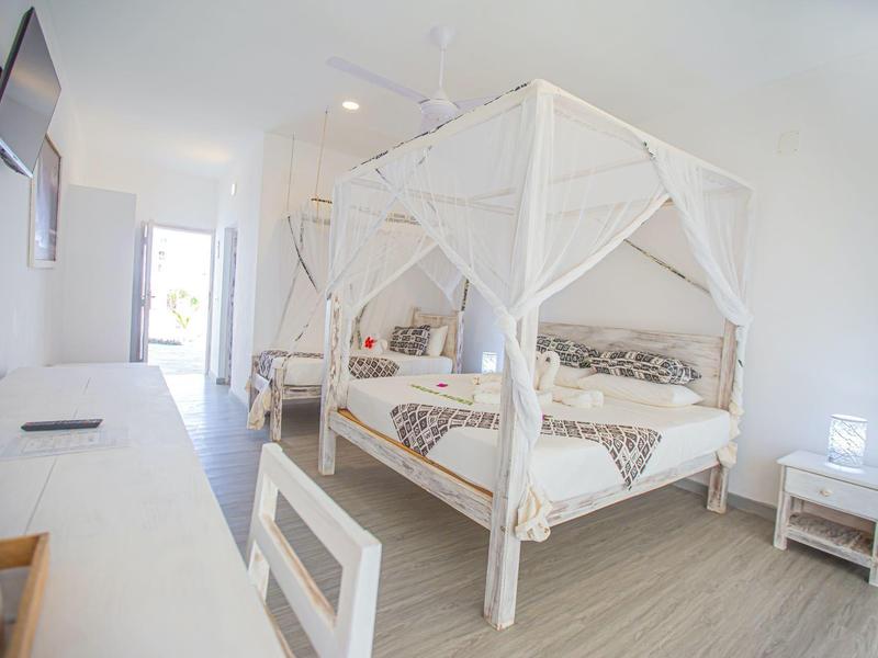 Chambre d'hôtel lumineuse avec lit à baldaquin, bureau, chaise et télévision murale.