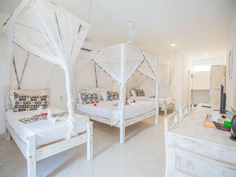 Chambre lumineuse avec deux lits, moustiquaires et décoration minimaliste.