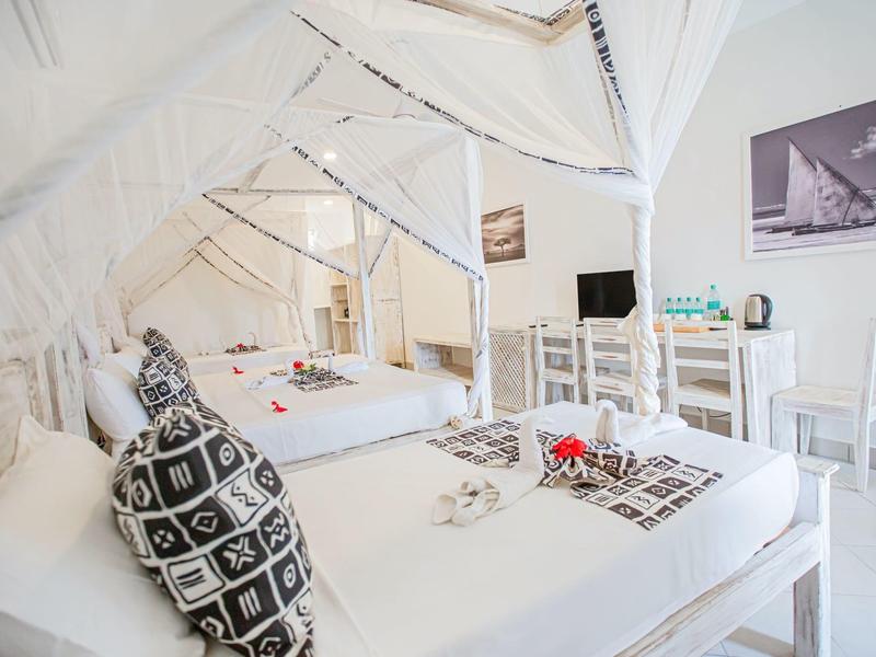 Chambre d'hôtel lumineuse avec mobilier blanc, coussins décoratifs et table avec chaises.