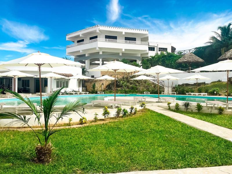 Hôtel moderne avec piscine, parasols et jardin bien entretenu sous un ciel ensoleillé.