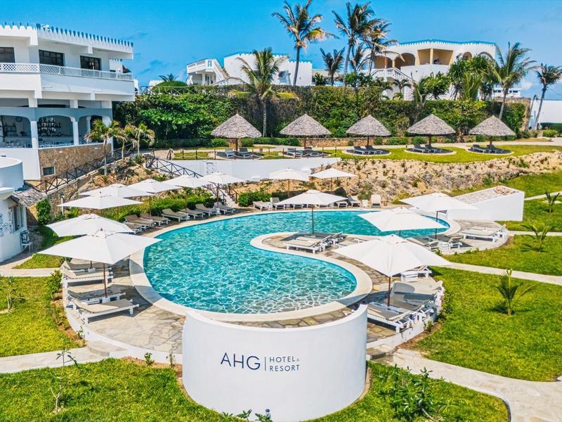 Complex hôtelier moderne avec piscines, parasols et pelouses vertes sous un ciel clair.