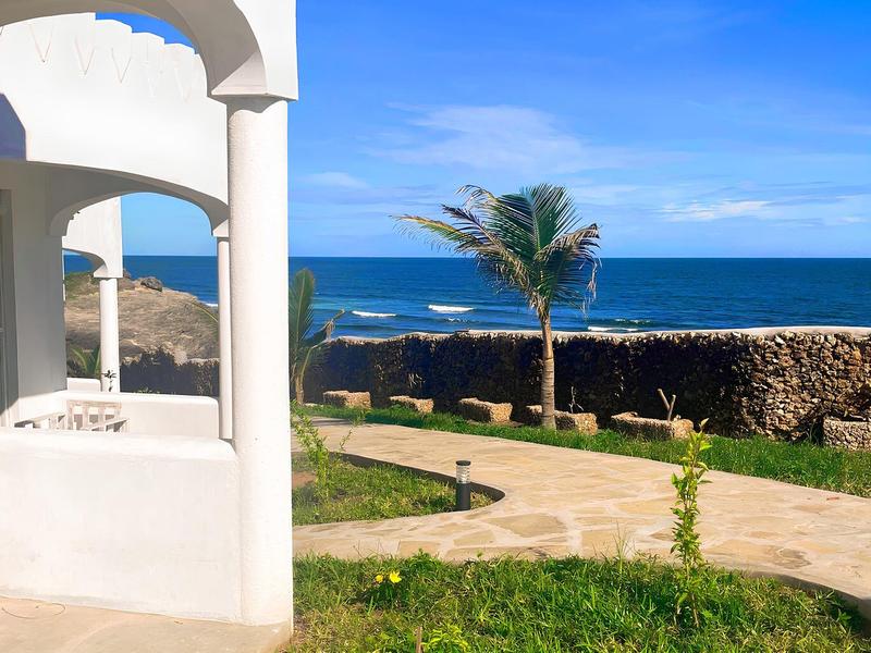 Un bâtiment d'hôtel blanc avec une arche et vue sur la mer et des palmiers sous un ciel bleu.