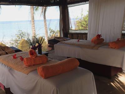 Massagebereich mit zwei Tischen unter offenem Pavillon, umgeben von tropischer Natur am Strand.