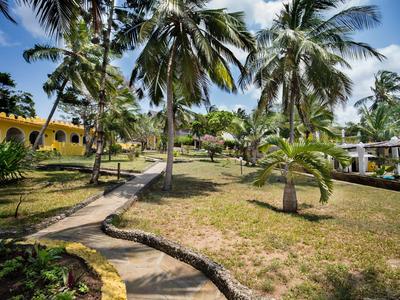 Hotelgarten mit Palmen, Gehwegen und gelben Gebäuden unter blauem Himmel.