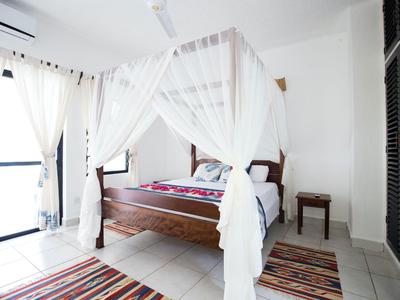 Helles Schlafzimmer mit Himmelbett, weißen Vorhängen und bunten Teppichen in einem Hotel.