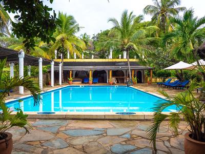 Schwimmbad mit klarem Wasser, umgeben von Palmen und Liegestühlen in einem tropischen Hotel.