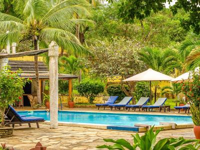 Ein ruhiger Poolbereich mit Liegestühlen, Sonnenschirmen und tropischer Begrünung in einem Hotel.