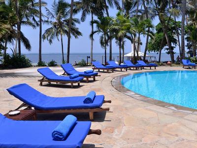 Varias tumbonas azules alrededor de una piscina con palmeras y vista al mar al fondo.