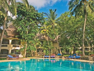 Hotel con piscina al aire libre y palmeras tropicales rodeado de tumbonas en clima soleado.