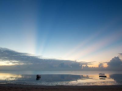 Playa al amanecer con mar tranquilo y nubes en el cielo.