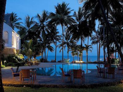 Acogedora zona de piscina por la noche con palmeras y vista al océano.