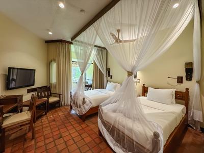 Habitación de hotel con dos camas individuales, mosquiteros, televisor de pantalla plana y escritorio.