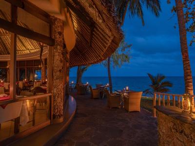 Abendliche Terrasse eines Hotels mit Sitzgelegenheiten und Blick auf das Meer unter blauem Himmel.