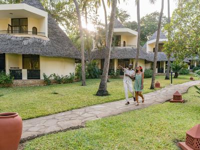 Zwei Personen spazieren auf einem Pfad zwischen tropischen Bungalows im Urlaubsresort.