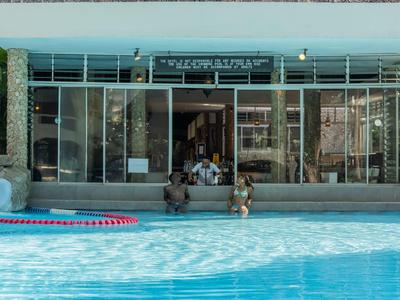 Moderner Hotelpool mit Blick auf den Eingang eines Gebäudes mit großen Glasfenstern.