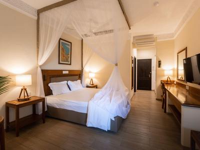 Modernes Hotelzimmer mit Doppelbett, Baldachin, Schreibtisch, Fernseher und warmem Licht.