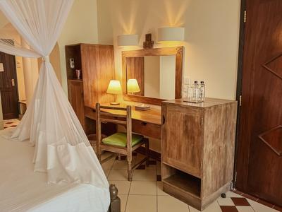 Helles Hotelzimmer mit Holzmöbeln, Schreibtisch, Sessel, Bett mit Moskitonetz und Tür.