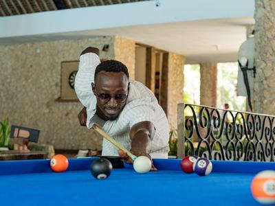 Ein Mann spielt Billard in einem hellen Raum mit blauer Spielfläche und konzentriertem Blick.