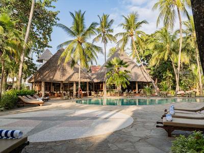 Ein tropisches Resort mit Pool, Palmen und Liegestühlen unter blauem Himmel.