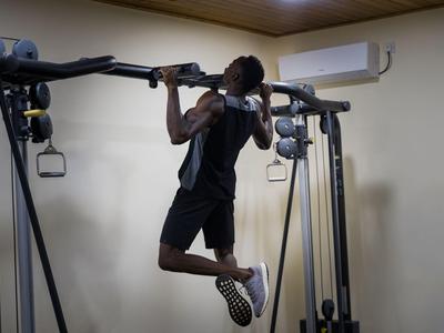 Ein Mann macht Klimmzüge an einem Fitnessgerät in einem Innenraum mit schlichter Wand.